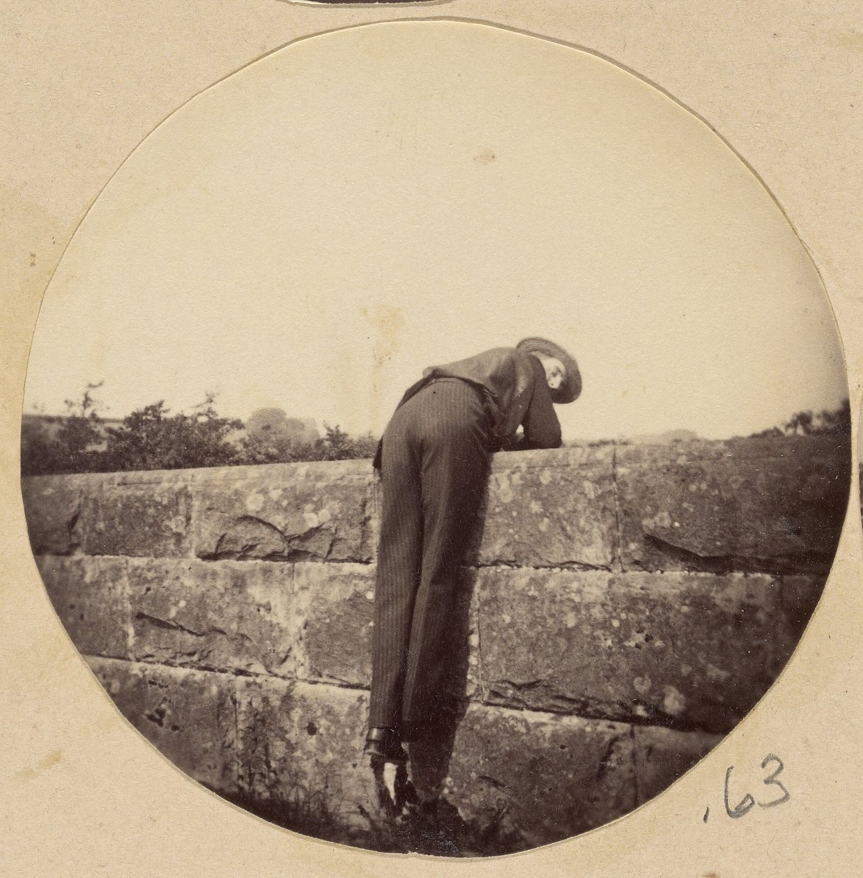 [Hombre con sombrero inclinado sobre un muro de piedra] de Unknown artist