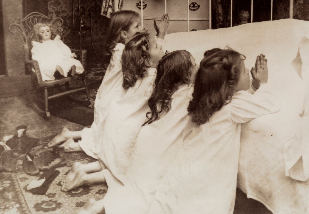 Cuatro niñas arrodilladas junto a una cama mientras rezan la oración de la tarde. de Unknown photographer
