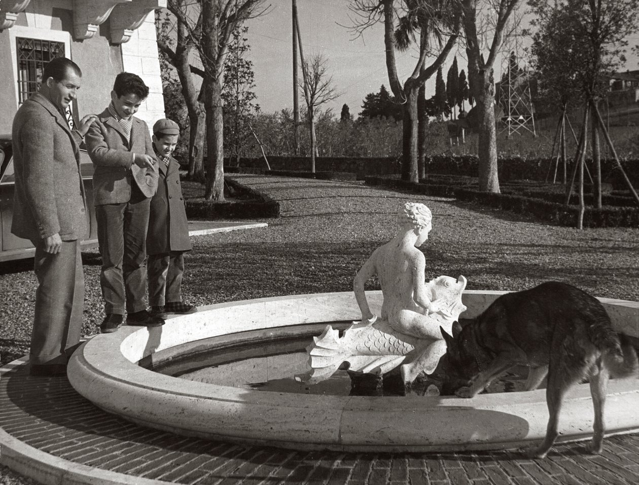 Gino Bartali con dos niños y un perro cerca de una fuente de Unknown photographer