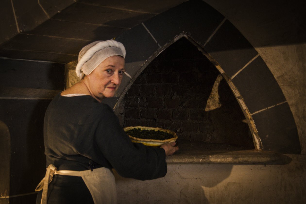 Recreación histórica: Doncella poniendo un pastel en el horno de la cocina del castillo de John Ward Dunsmore