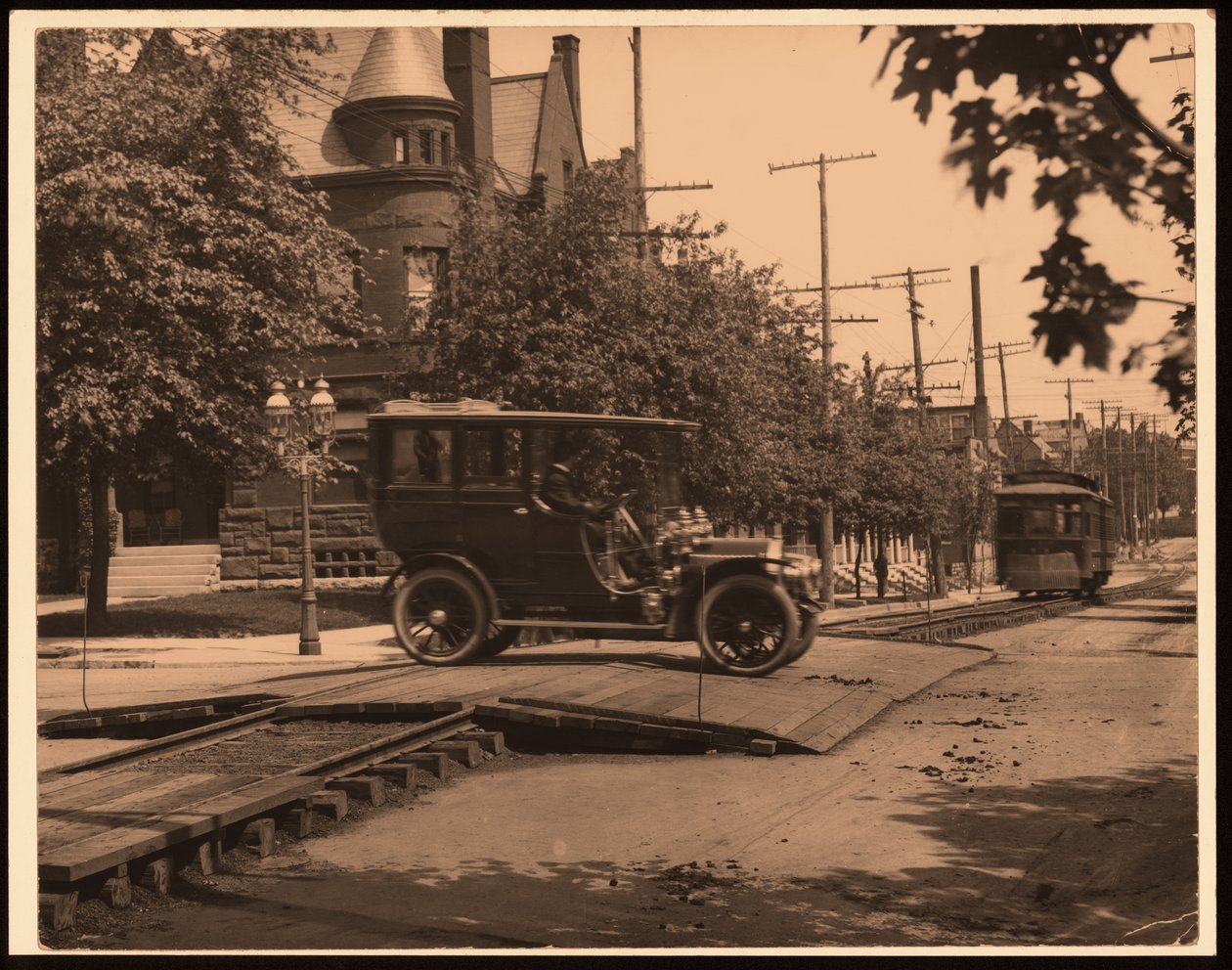 Fotografía horizontal en blanco y negro de un automóvil cruzando las vías del tranvía mientras un tranvía se mueve por la vía de William G. Swekosky