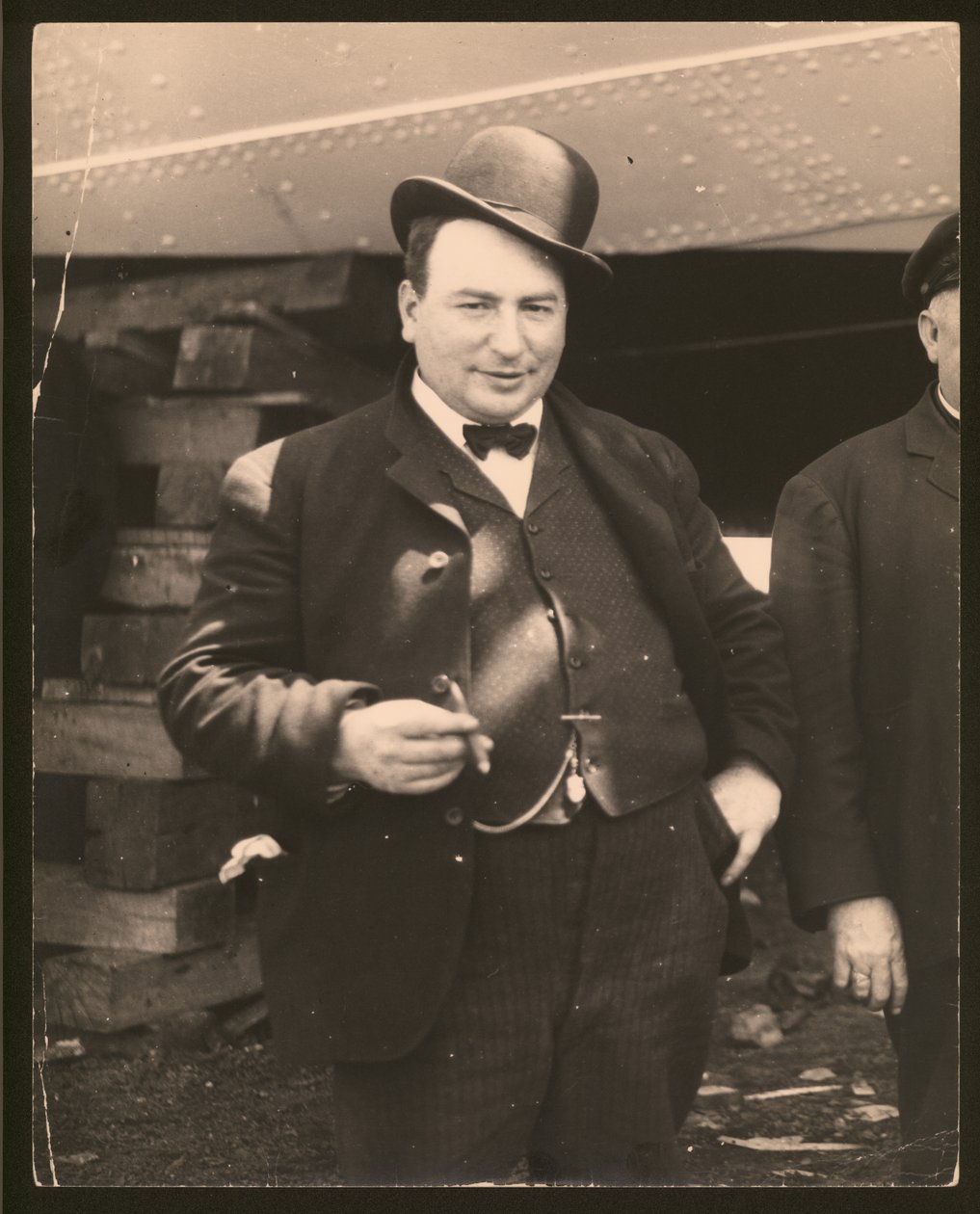 Fotografía vertical en blanco y negro de un hombre con sombrero hongo y pajarita fumando un cigarro de William G. Swekosky