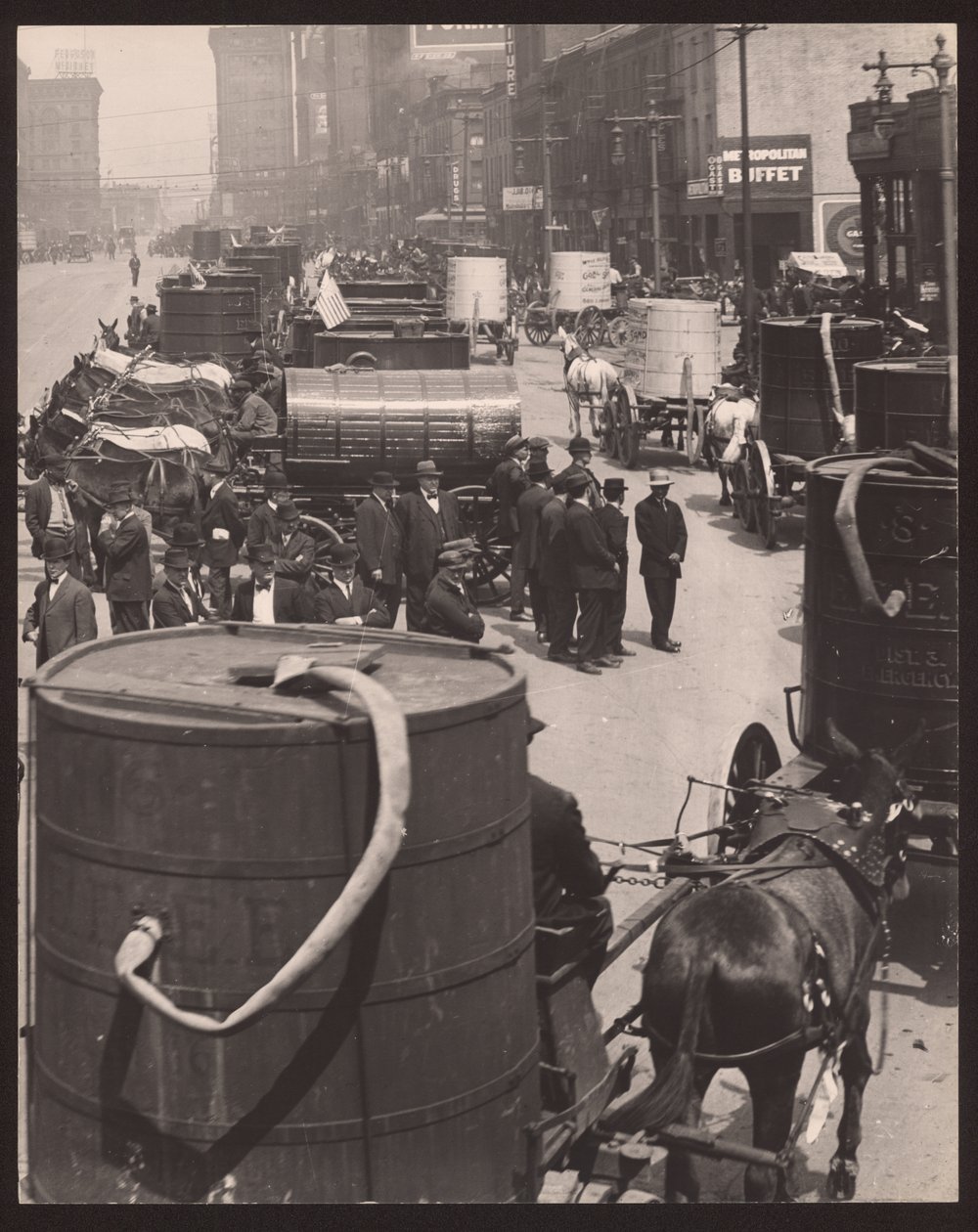 Fotografía vertical en blanco y negro de una fila de carros tirados por caballos llevando barriles de agua. Un grupo de hombres está de pie frente a la fila de William G. Swekosky