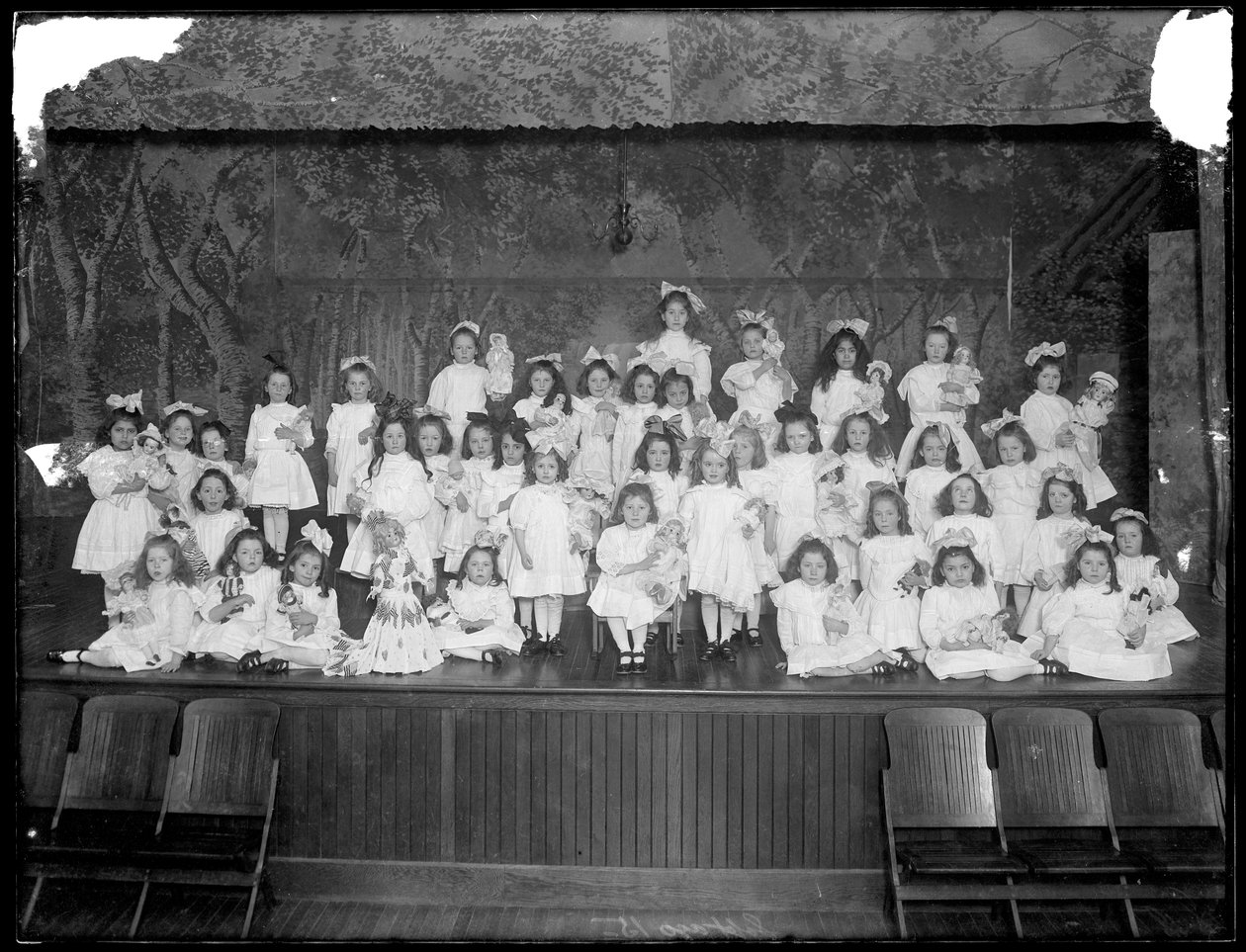 Grupo de niñas pequeñas posando en un pequeño escenario sosteniendo muñecas, probablemente el Asilo de Huérfanos Católicos Romanos, Kingsbridge, Bronx, c.1911 de William Davis Hassler