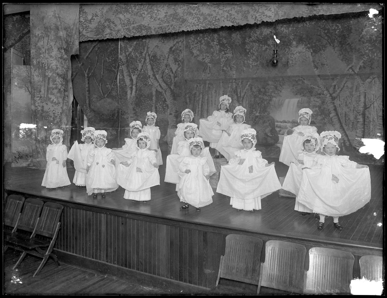 Niños de jardín de infantes en el escenario: niñas muy pequeñas actúan en un pequeño escenario, probablemente el Asilo de Huérfanos Católico Romano, Kingsbridge, Bronx, c.1911 de William Davis Hassler