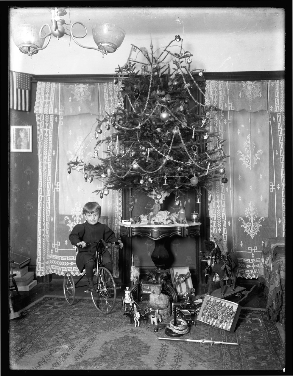 Niño Seymour posando sentado en triciclo junto al árbol de Navidad en el salón, Navidad 1912 de William Davis Hassler