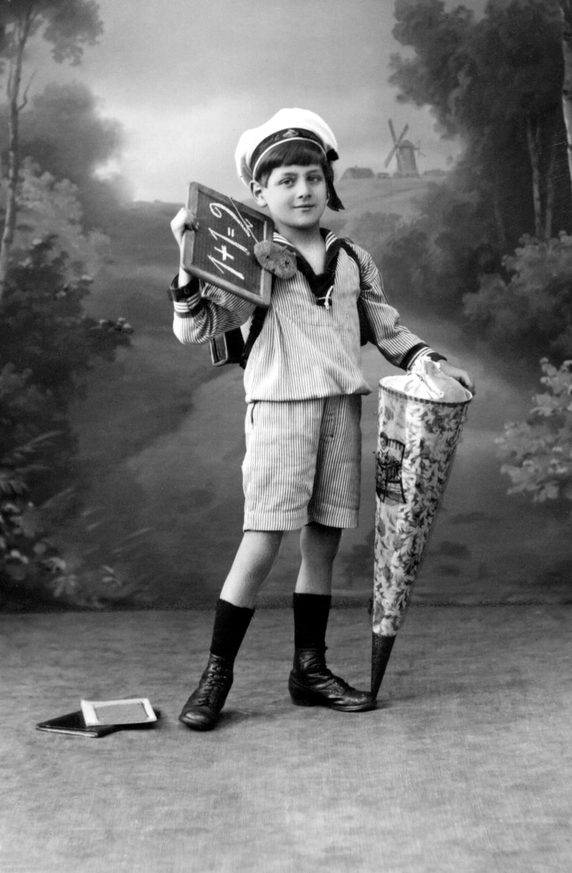 Primer día de escuela. Un niño en uniforme posando con una pizarra mostrando la suma 1+1 = 2 y una bolsa sorpresa. Fotografía alrededor de 1910. de Ferdinand Georg Waldmuller