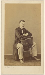 [Hombre con bigote, sentado, con la parte delantera hacia atrás de la silla con flecos]