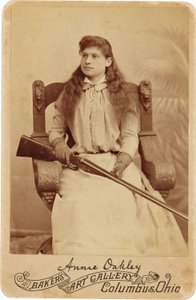 Annie Oakley : Annie Oakley:. Aquí, la legendaria tiradora está sentada con bastante recato en una enorme silla de estilo renacentista, con una escopeta en el regazo. Sus delicados rasgos femeninos y su cabello suelto desmienten su robusta imagen al aire l de American Photographer