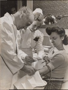 [Médico y enfermera insertan una aguja en el brazo de una mujer] de Arnold Eagle