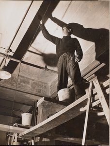 [Hombre de pie sobre un andamio de madera pinta un techo] de Arnold Eagle