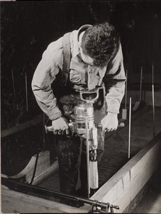 [Un hombre utiliza una máquina manual para trabajar con un trozo de madera]. de Arnold Eagle
