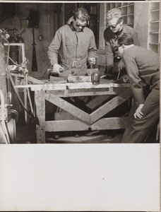 [Tres hombres con gafas sueldan una pieza de metal sobre una mesa] de Arnold Eagle