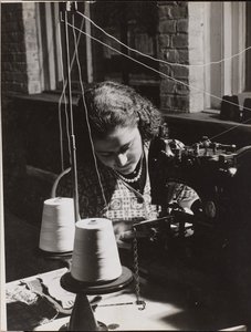 [La mujer utiliza una máquina de coser enhebrada con dos carretes de hilo blanco] de Arnold Eagle