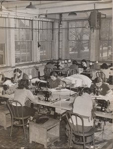 [Mujeres sentadas en escritorios trabajan en máquinas de coser] de Arnold Eagle