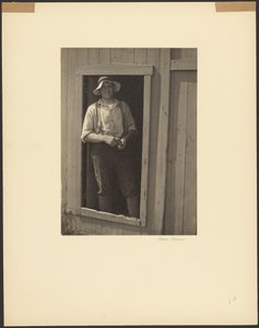 [Hombre con sombrero de paja de pie en la puerta de un granero sosteniendo una bolsa de tabaco] de Doris Ulmann