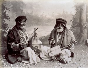 Retrato de dos músicos árabes con vestimenta étnica humilde. Los hombres mayores están posando en el estudio, sentados en el suelo. Detrás de ellos hay un fondo de un paisaje boscoso de Félix Bonfils