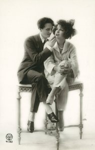 Hombre andrógino en traje aplicando lápiz labial a chica en pijama de French Photographer