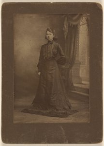 [Retrato de una mujer joven con vestido negro largo, de pie]
