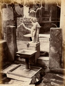 Una fuente compuesta por una escultura de un niño desnudo. La fuente está en la Casa del Balcón colgante, en Pompeya de Giorgio Sommer