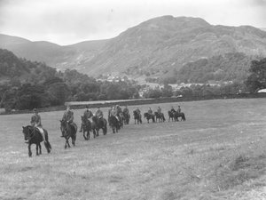 Un grupo de hombres caminando en fila sobre ponis, los fells al fondo