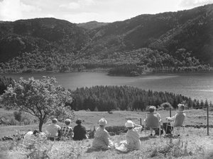 Grupo de personas sentadas en la hierba o en tumbonas mirando una vista de Thirlmere de Joseph Hardman
