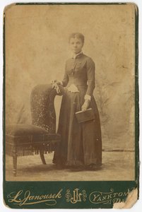 Fotografía de una mujer de pie junto a una silla y sosteniendo un libro, finales del siglo XIX de Louis Janousek