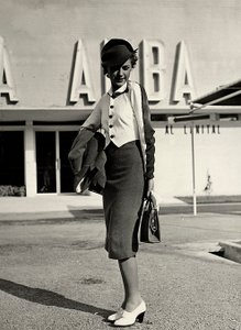 Modelo lleva conjunto creado por la casa de alta costura "Graldi". El atuendo se compone de un traje con blusa de dos tonos. Un sombrero rígido completa el conjunto.