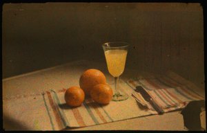 Fotografía en color de un bodegón de naranjas frescas y un vaso de zumo de naranja tomada con...