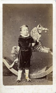 Niño pequeño de pie junto a un caballo de juguete de Silas Eastham