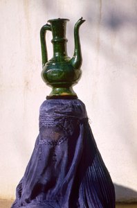 En Kabul, una mujer oculta por un chadri (chador) de seda lleva una jarra...