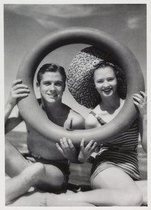 Hombre y mujer mirando a través de un aro de goma en la playa, c 1935