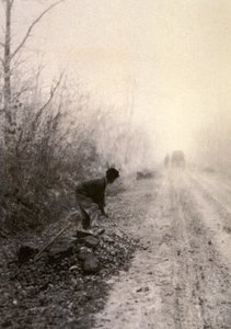 Un camino rural envuelto en la bruma matinal. En primer plano un hombre parte piedras de Unbekannter Künstler
