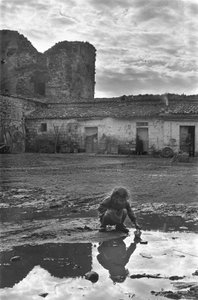 Niña joven jugando con un barco de papel en un charco rodeado de barro, Venosa, Basilicata, Italia de Unbekannt