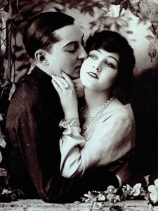Retrato de medio cuerpo de una joven pareja apoyada en un balcón decorado con plantas. El hombre rodea a la chica por la cintura y le besa la mejilla. de Unknown photographer