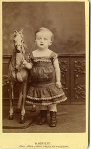 Niña de pie junto a caballo de balancín de W. Hoffert