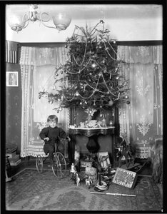 Niño Seymour posando sentado en triciclo junto al árbol de Navidad en el salón, Navidad 1912