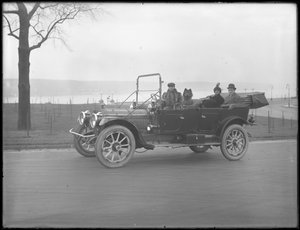 Tres personas no identificadas y dos perros Chow conduciendo en un coche convertible a lo largo de un río o lago, c.1912 de William Davis Hassler