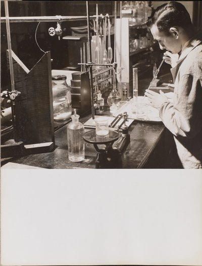 [Un hombre en un laboratorio utiliza ambas manos para colocar una gran pipeta en un vaso de precipitados]. de Arnold Eagle