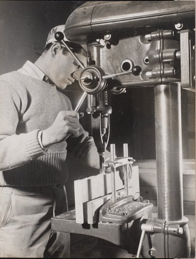 [Hombre utiliza una máquina para perforar agujeros en dos bloques de madera] de Arnold Eagle