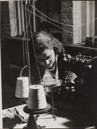 [La mujer utiliza una máquina de coser enhebrada con dos carretes de hilo blanco] de Arnold Eagle