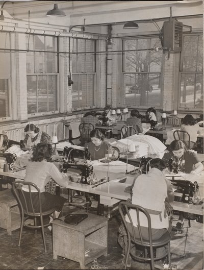 [Mujeres sentadas en escritorios trabajan en máquinas de coser] de Arnold Eagle