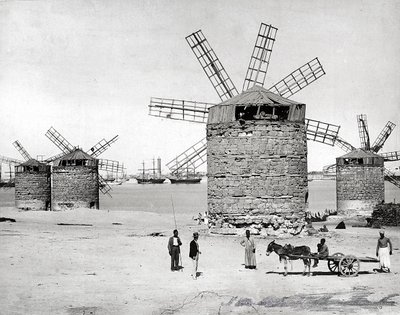 Molinos de viento en el mar Mediterráneo en Alejandría, Egipto. Delante, unos egipcios posando con un pequeño carro. de Brothers Zangaki