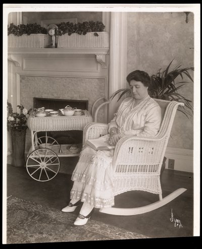 La Sra. Howard sentada con un libro en una mecedora en su casa en 200, 5th Avenue, Nueva York, 1915-6 de Byron Company