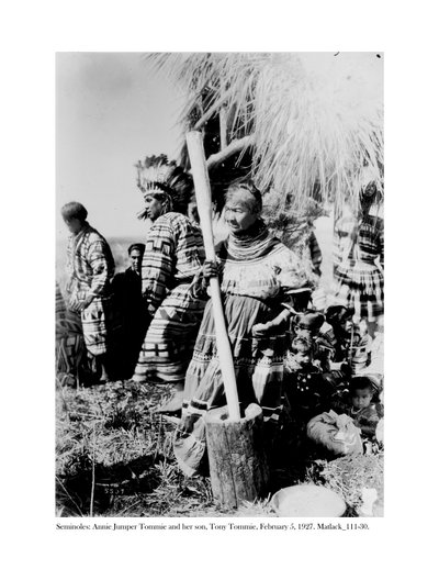 Annie Jumper Tommie usando un mortero y pilón para hacer harina de maíz, y su hijo, Tony Tommie, con un tocado de plumas de águila, 5 de febrero de 1927 de Claude C. Matlack