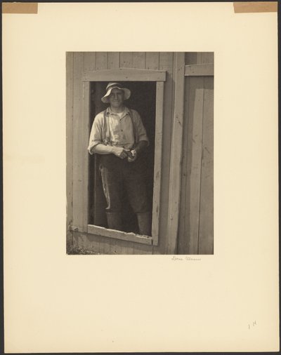 [Hombre con sombrero de paja de pie en la puerta de un granero sosteniendo una bolsa de tabaco] de Doris Ulmann