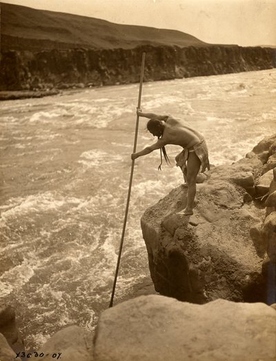 Indio tlakluit, de pie sobre una roca, pescando con una red, hacia 1910 (fotografía en blanco y negro). de Edward Sheriff Curtis