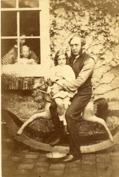 Padre e hija sentados en un caballo mecedor con el hermano y la madre mirando por la ventana, 1860s de English Photographer