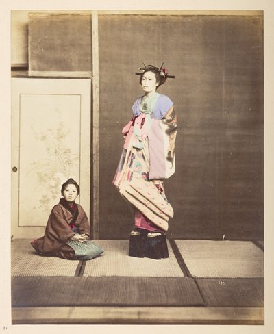 [? Geisha, ] Retrato de estudio de pie de cuerpo entero de una mujer joven con zapatos elevados, su joven asistente arrodillada en el suelo junto a ella,   Fotógrafo: Desconocido  Colección Lucas: Registro fotográfico de la gira mundial de Charles James y  de English Photographer