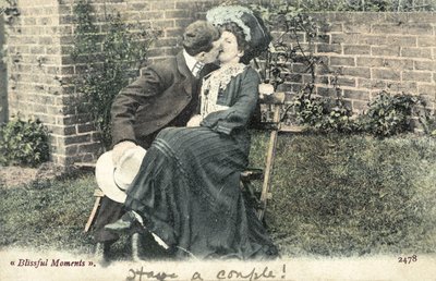 Hombre robando un beso a una chica en un banco de jardín de English Photographer